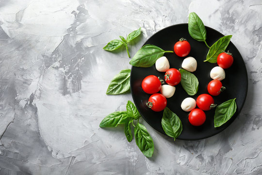 Mozzarella cheese balls, cherry tomatoes and green fresh organic basil on grey background