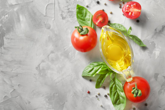 Composition with oil, cherry tomatoes and green fresh organic basil on grey background