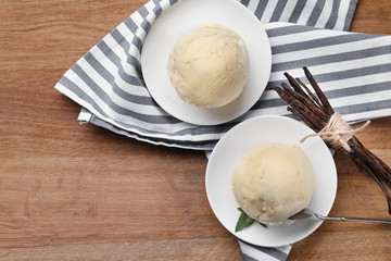 Plates with delicious vanilla ice cream on wooden background