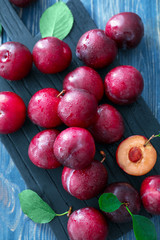 Board with fresh ripe plums on wooden table