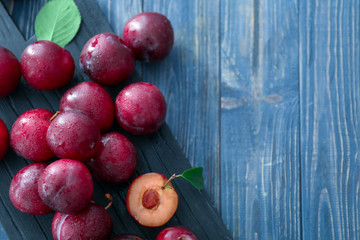 Board with fresh ripe plums on wooden table