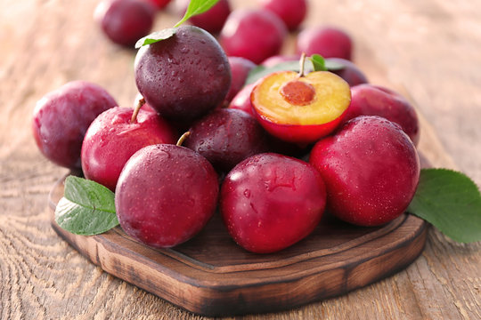 Board with fresh ripe plums on wooden table, closeup