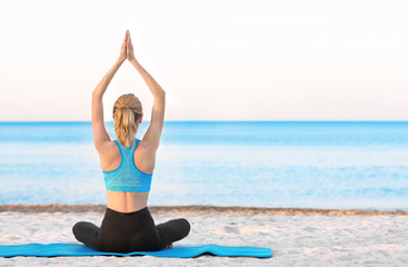 Fototapeta na wymiar Beautiful young woman practicing yoga on sea beach