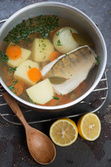 Fresh fish soup with sudak and vegetables in a kettle, high angle view, vertical shot