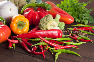 Harvest of different peppers and vegetables on a wooden background