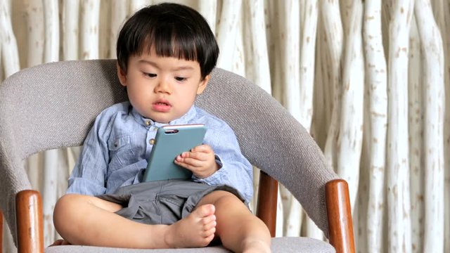 Asian little boy sitting on chair and holding mobile phone