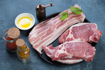 Raw fresh bacon and pork meat steaks with seasonings, horizontal shot, selective focus