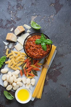Above view of bolognese sauce with different types of raw pasta, gnocchi and other cooking ingredients, vertical shot with space