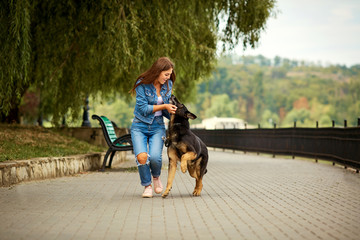A young girl is walking with a German shepherd dog in the park.