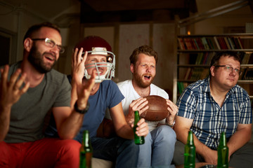 Four friends watching american football game on television, feeling frustrated
