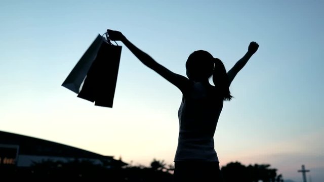 Slow motion of Silhouette excited woman holding shopping bags at sunset time with sky background