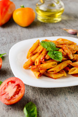 Penne with tomato sauce and basil on wooden background