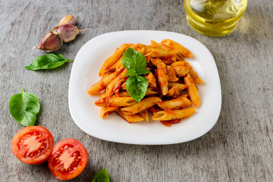 Penne with tomato sauce and basil on dark background, top view.