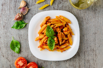 Penne with tomato sauce and basil on wooden background, top view.