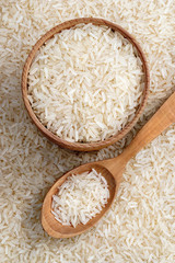Wooden bowl and spoon with parboiled rice on background of scattered rice. Top view. High resolution product