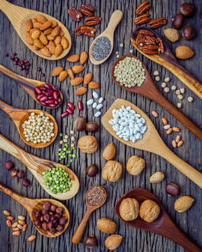 Various legumes and different kinds of nutshells in spoons. Walnuts kernels ,hazelnuts, almond ,brown pinto ,soy beans ,flax seeds ,chia ,chickpea ,red kidney beans and pecan on shabby wooden table.