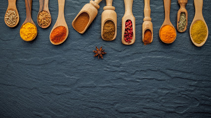 Various of Indian spices and herbs in wooden spoons. Flat lay of spices ingredients chilli ,pepper, garlic,dries thyme, cinnamon and star anise on the black stone.