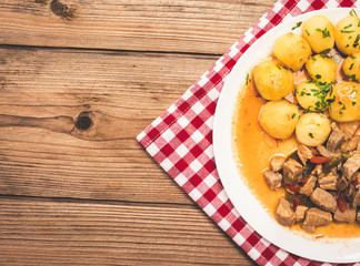 Goulash with meat, vegetables and potatoes on wooden table.