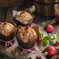 A festive breakfast. Fragrant fruitcakes in brown paper forms with berries of lingonberry on wooden background with berries, New Year red balls. Selective focus