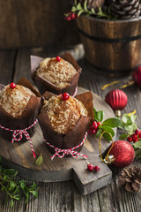 A festive breakfast. Fragrant fruitcakes in brown paper forms with berries of lingonberry on wooden background with berries, New Year red balls. Selective focus