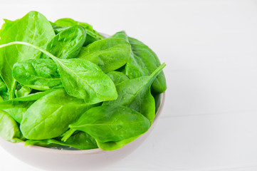 Fresh spinach leaves with water drops in ceramic bowl on thw white wooden background. Selective focus. Space for text