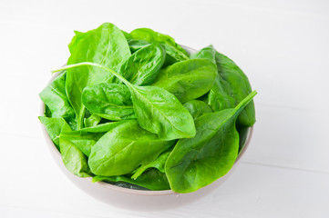 Fresh spinach leaves with water drops in ceramic bowl on thw white wooden background. Selective focus. Space for text