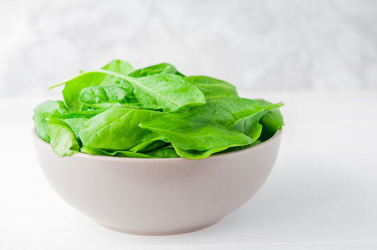 Fresh spinach leaves with water drops in ceramic bowl on thw white wooden background. Selective focus. Space for text
