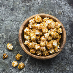 A wooden bowl with caramelized popcorn on a gray grunge trend background. Top View.