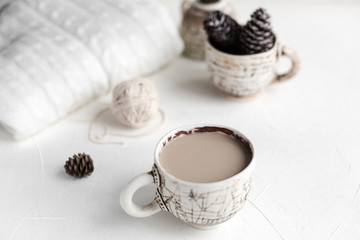 A cup of coffee with milk and a cosy wool plaid on the white concrete table in the morning. Winter or autumn season.