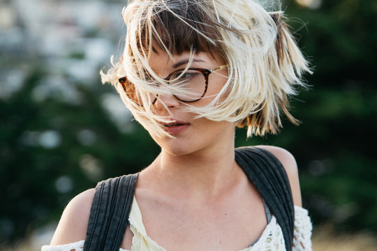 close portrait of young female woman girl wearing glasses with hair blown in city park