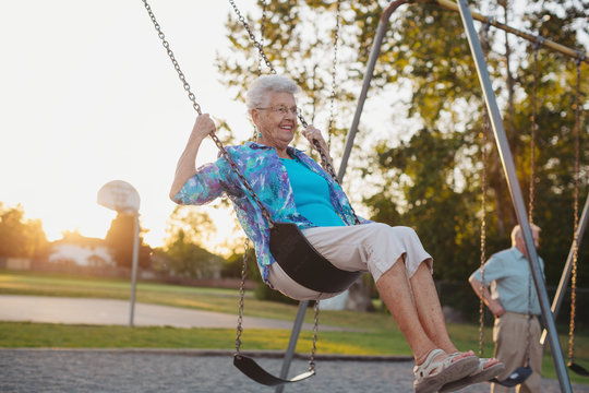 Two happy, senior caucasian friends swinging together on swingset at sunset