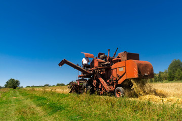Old red combine harvester working in a wheat field.