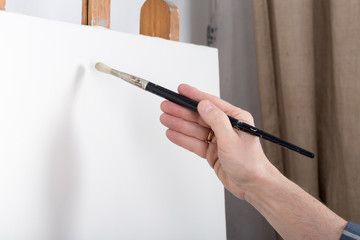 An artist in studio thinking in front of white canvas