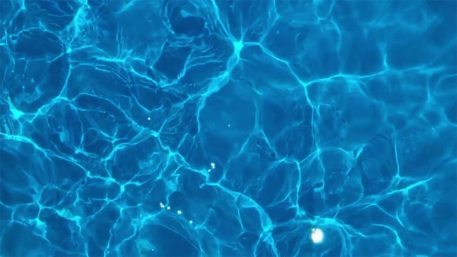 Pure blue water in the pool with light reflections. Slow motion.