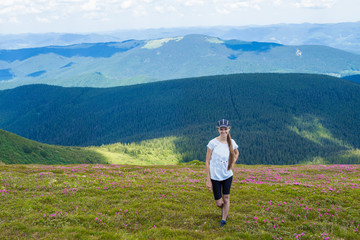 Fototapeta na wymiar Young woman Hiking at Carpathians Mountains stands on top of a hill, against a backdrop of beautiful mountains and a blue sky
