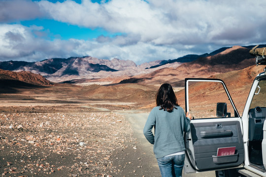 woman on a road trip standing outside her car looking at a rugged mountain landscape