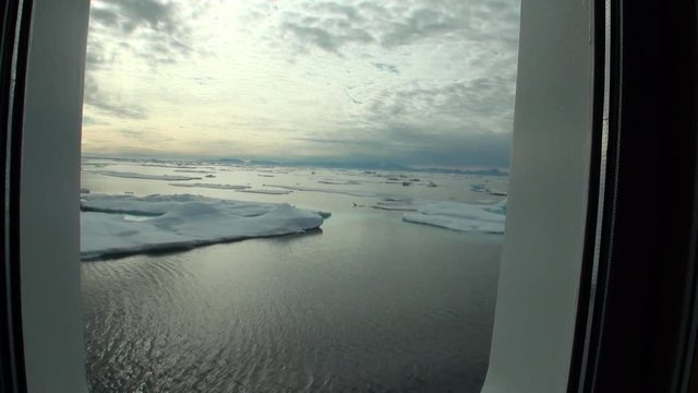 Ice and iceberg from porthole window of yacht in Arctic Ocean. Extreme tourism and travel in the cold polar north. Scenic picturesque and blue water on background of snowy mountains.