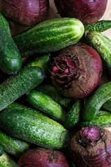 Close up of freshly harvested pickling cucumbers and beetroots on light wooden board from above.