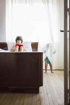 5 year looking a digital tablet while his brother hidding behing a curtain