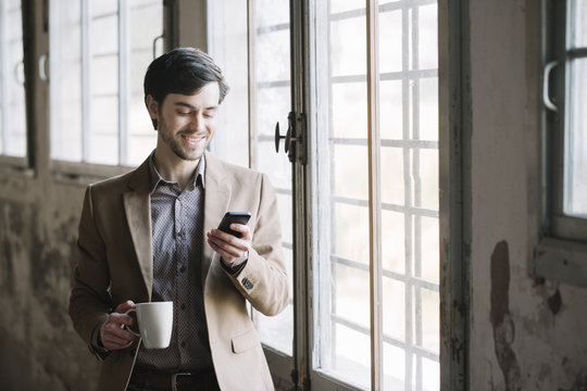 Elegant man with cup of coffee using cell