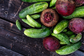 Freshly harvested pickling cucumbers and beetroots on dark rustic wooden board from above. Space for text.