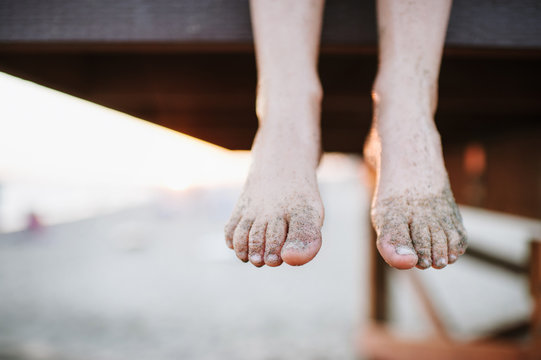 Child's feet hanging off lifeguard stand with sandy feet
