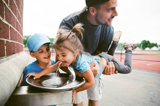 dad helps little girl get drink from fountain