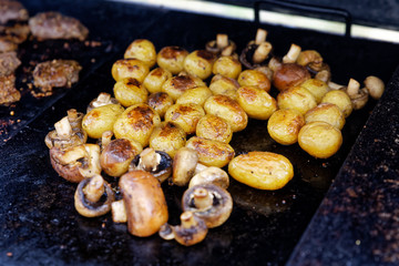 Grilled button mushrooms and whole potatoes on outdoor grill.
