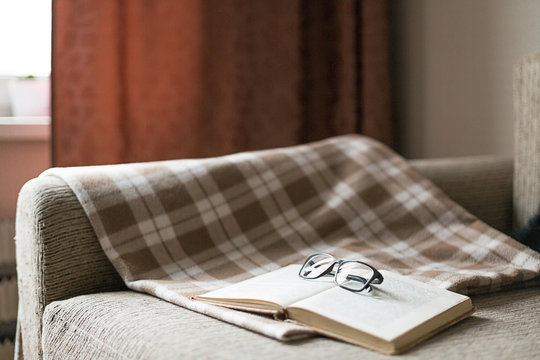 A cozy sofa, a  pillow and a plaid, open book and glasses. Leisure time, reading and resting.
