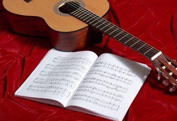 Fototapeta na wymiar acoustic guitar and music notes on red velvet fabric, close view of objects