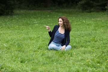 Fototapeta premium A young woman is sitting on the grass and pointing at something with her finger