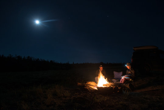 Couple reading by campfire with full moon
