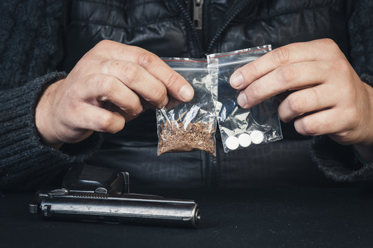 Young man sitting at the table with arms holding packages with drugs.