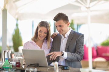 Couple of young business people is using laptop while sitting and relaxing at the bar